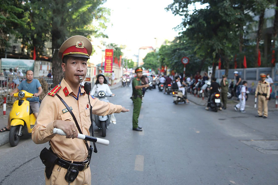 CSGT vừa điều tiết giao thông, vừa phát tờ rơi tuyên truyền đến phụ huynh, học sinh trong ngày khai giảng. Ảnh: Tô Thế