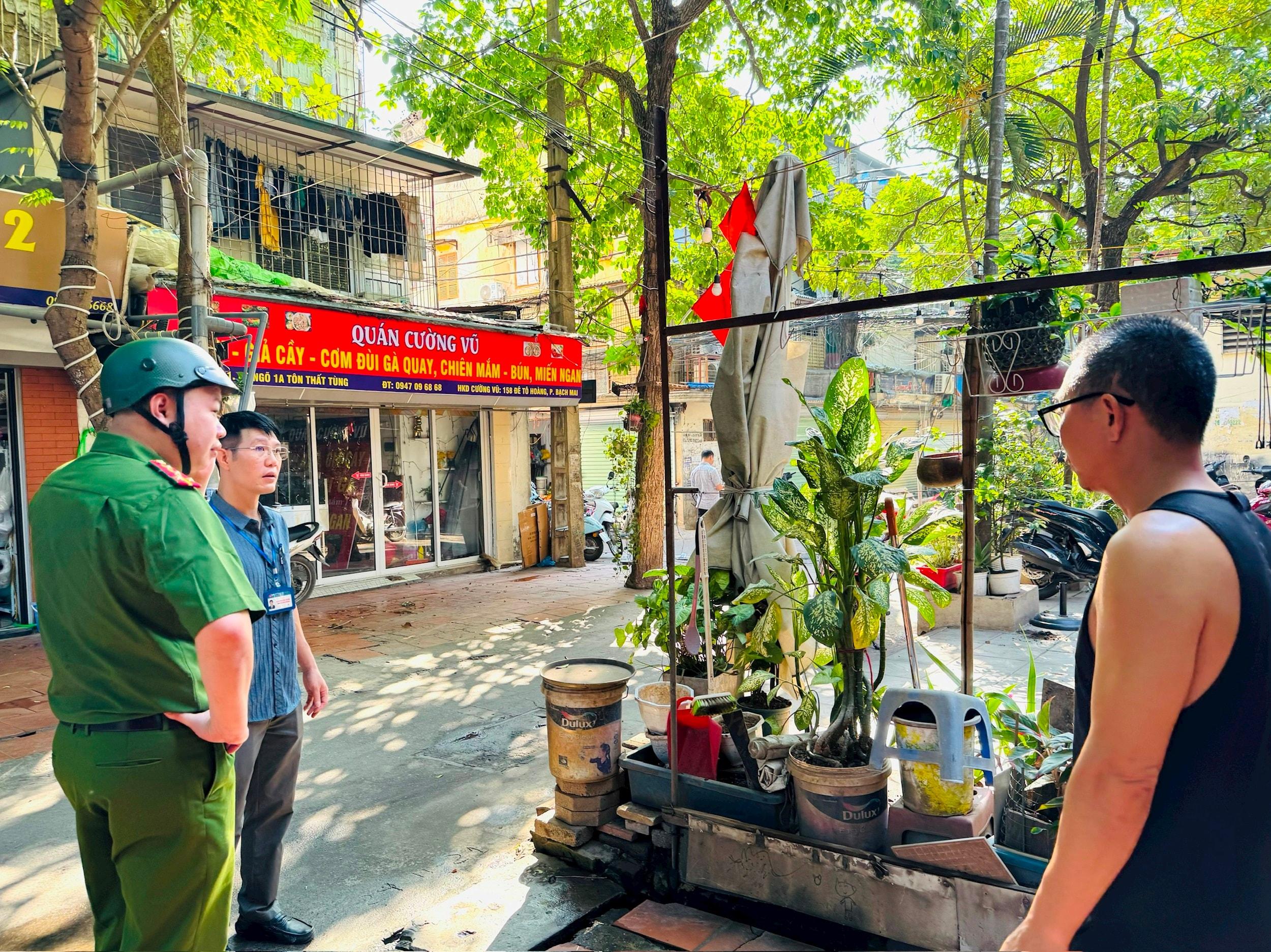 Lực lượng chức năng phường Kim Liên nhắc nhở, tuyên truyền việc dọn dẹp chậu cây, vật dụng cản trở lối đi của người dân. Ảnh: PV