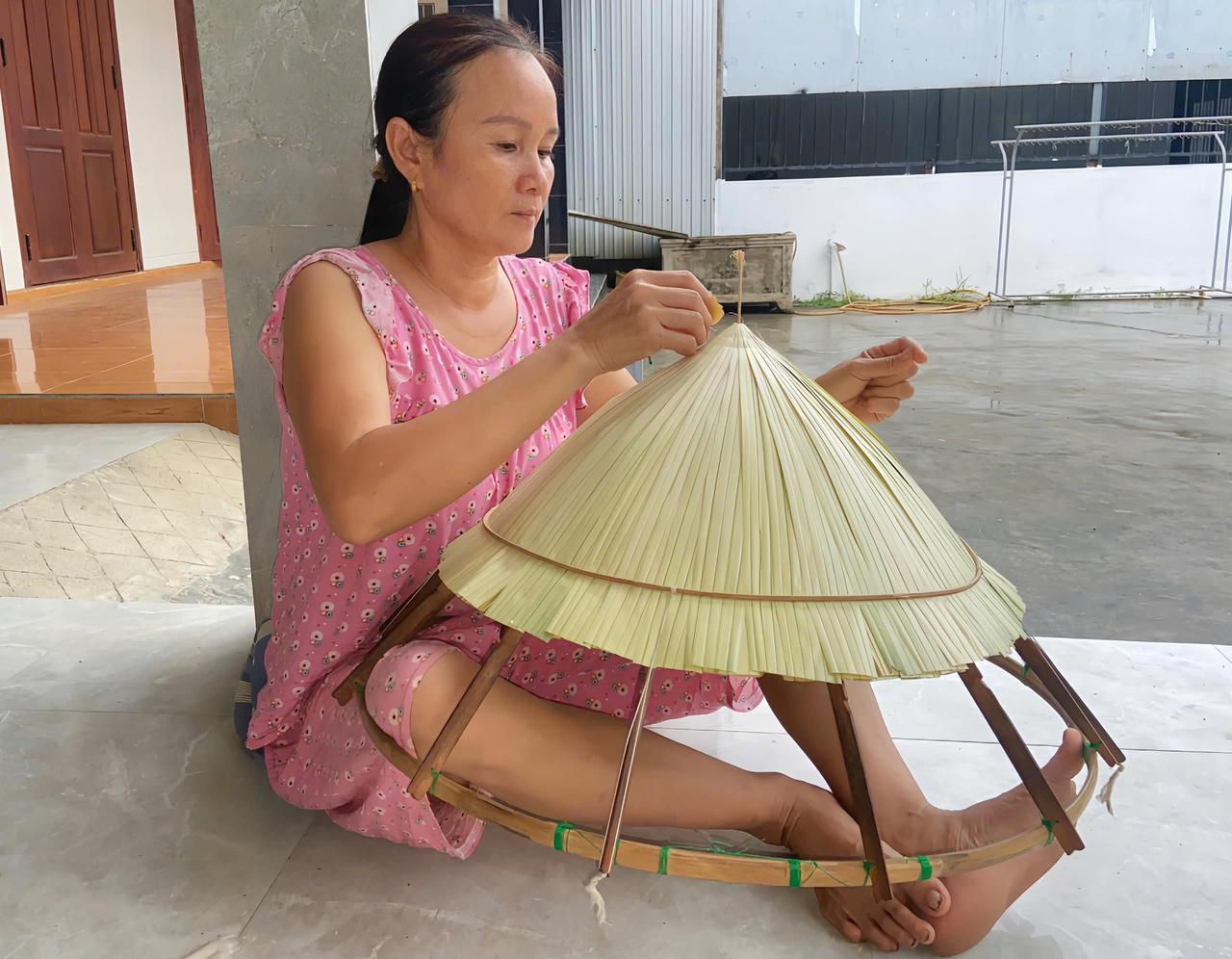 Bà Trương Thị Vẩn thực hiện công đoạn lợp lá, một trong những khâu đòi hỏi sự khéo léo để từng tàu lá được xếp đều, tạo nên độ kín và vẻ đẹp cho chiếc nón.